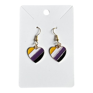 May include: Heart-shaped earrings with a non-binary pride flag design. The earrings have gold-coloured hooks and heart pendants with yellow, white, purple, and black stripes. They are displayed on a white card.