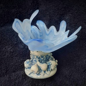 May include: A blue glass bowl with a white base decorated with pears. The bowl is shaped like a flower and has a wavy, organic design.