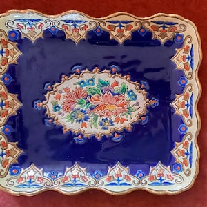 Könnte beinhalten: Eine blaue und weiße Keramik-Servierplatte mit gewelltem Rand und floralem Muster. Die Platte hat einen goldenen Rand und einen weißen Hintergrund mit einer blauen Mitte. Das Blumenmuster zeigt rote, rosa und gelbe Blumen.