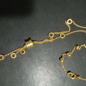 May include: A gold necklace with a layered chain design. The necklace features a round pendant with multiple rings and a smaller chain with round charms.