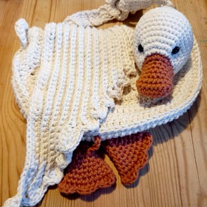 May include: Handmade crochet goose-shaped bag in cream and orange. The bag features a white goose head with black eyes and an orange beak. The body of the bag is cream-colored with a scalloped edge and orange feet.