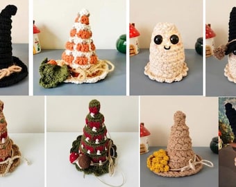 Puede incluir: Una colección de objetos de ganchillo que incluye sombreros de bruja negros con escobas pequeñas, conos con motivos de calabaza naranjas y blancos, fantasmas color crema con ojos negros y formas cónicas decoradas con setas rojas y detalles de hilo.