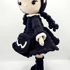 May include: A crocheted doll with black hair, a black dress with white trim, and black boots. The doll has a white face with black eyes.