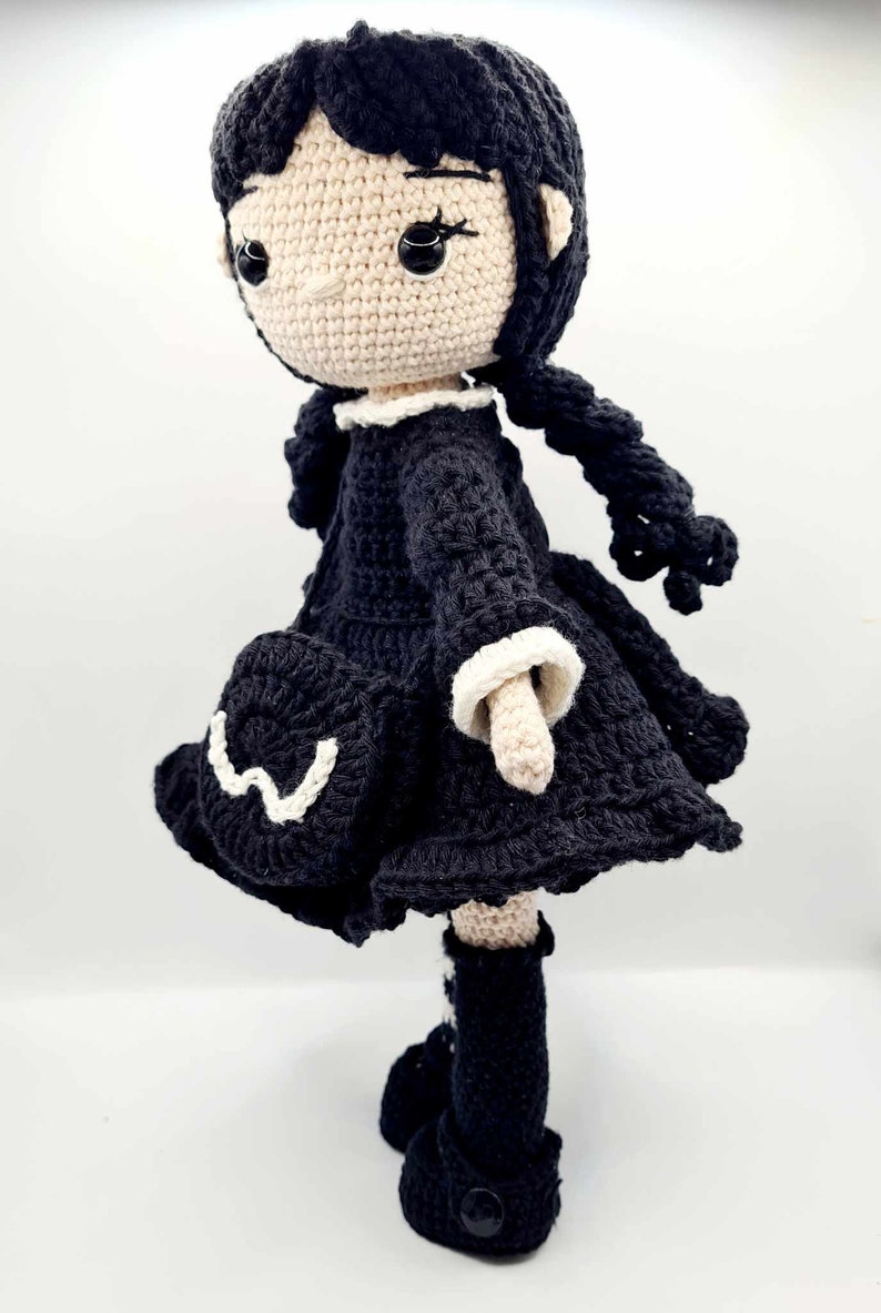 May include: A crocheted doll with black hair, a black dress with white trim, and black boots. The doll has a white face with black eyes.