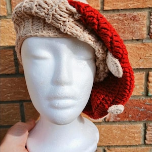 May include: A crocheted beret featuring a beige ribbed brim and a vibrant red crown. The red section is adorned with small, circular beige patches that resemble spots, creating a textured appearance on the surface of the headwear.