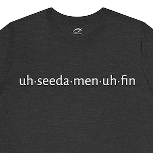 May include: Dark gray t-shirt with the text "uh.seeda.men.uh.fin" printed in white. The shirt has a crew neck and short sleeves. The fabric appears to be a soft, comfortable material.