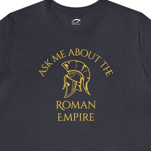 May include: Dark heather grey t-shirt with a gold graphic of a Roman helmet and the text "Ask me about the Roman Empire".