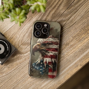 May include: A phone case with a close-up image of a bald eagle with its head turned to the side. The eagle is partially obscured by an American flag. The phone case has a camera lens cutout.