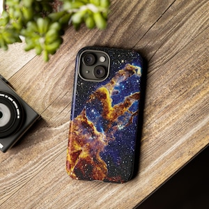 May include: A phone case with a galaxy-themed design featuring a nebula with orange, yellow, and blue colors. The case has a black background with a subtle sparkle effect.