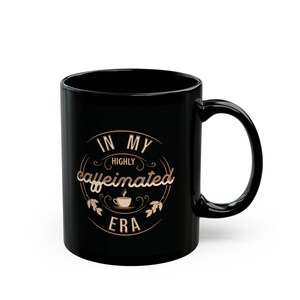 May include: Black coffee mug with a gold design that says "In My Highly Caffeinated Era".