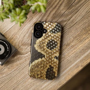 May include: A phone case with a snakeskin pattern in shades of brown, black, and gold. The case has a raised camera bump with two lenses.