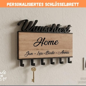 Könnte beinhalten: Ein rechteckiges Schlüsselbrett aus Holz mit heller Eichenoptik und schwarzen Metallelementen. Auf der Vorderseite steht der schwarze Schriftzug "Home" sowie die Namen "Jan - Lea - Bodo - Anna". Darunter befinden sich sechs schwarze Haken.