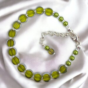 May include: A green glass bead bracelet with a silver chain clasp. The beads are round and have a slightly iridescent finish.