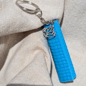 Peut inclure: Un porte-clés en forme de tapis de yoga bleu avec un charme de lotus argenté et un anneau de clé argenté.