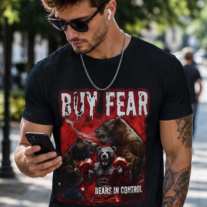 May include: A black short-sleeve t-shirt featuring a graphic print of three bears, one wearing red boxing gloves, set against a red background. The text "BUY FEAR" appears in white at the top, and "BEARS IN CONTROL" is printed in white at the bottom.