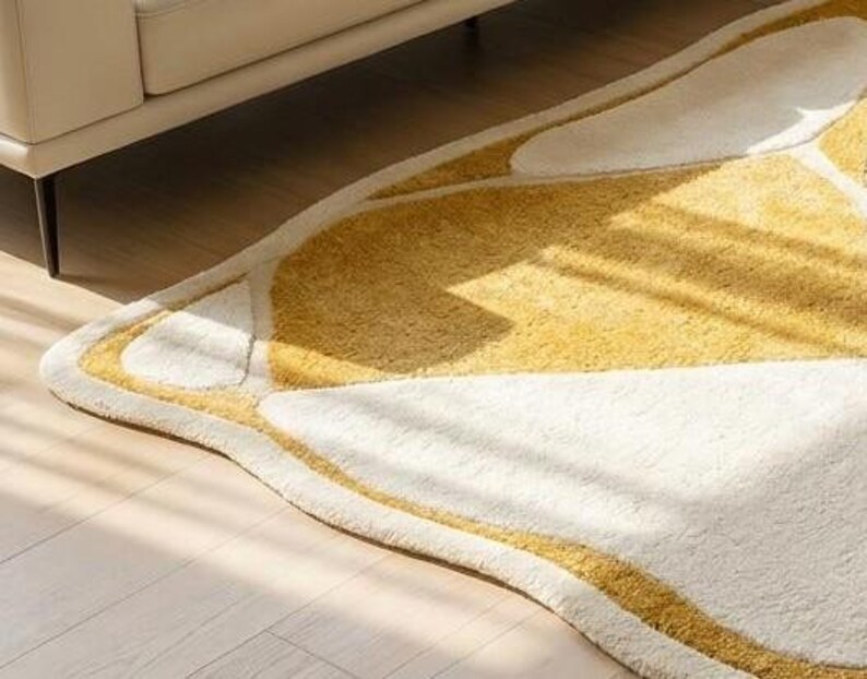 Pu&ograve; includere: Un tappeto morbido e astratto con un design a forma di farfalla. Il tappeto presenta una combinazione di tonalit&agrave; bianche e gialle, con un bordo giallo. Il tappeto &egrave; posizionato su un pavimento in legno chiaro, con una porzione di un divano beige visibile sullo sfondo.