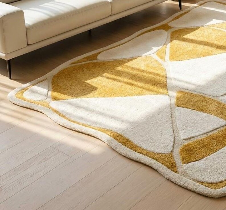 Pu&ograve; includere: Un tappeto a forma di foglia dal design moderno. Presenta un motivo di forme geometriche bianche e gialle, bordate di giallo. Il tappeto &egrave; posizionato su un pavimento in legno chiaro, con un divano bianco sullo sfondo.