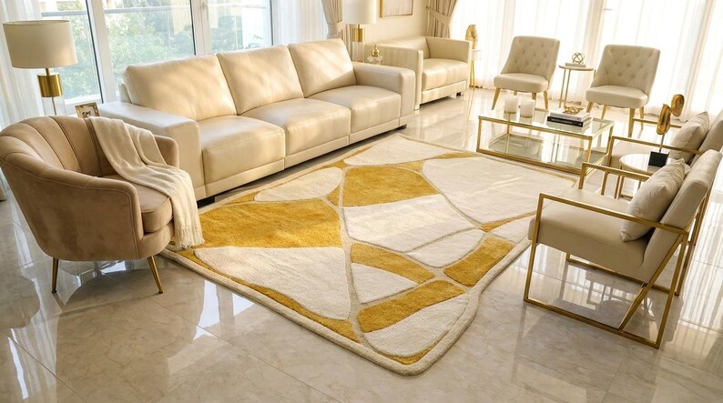 Pu&ograve; includere: Un soggiorno moderno con mobili color crema, tra cui un ampio divano, poltrone e un tappeto fantasia con forme geometriche gialle e bianche. Un tavolino in vetro con cornici dorate e dettagli dorati completano l'elegante design.