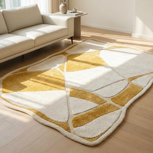 Pu&ograve; includere: Un moderno tappeto con un design astratto. Il tappeto presenta un motivo di forme bianche e giallo senape delineate da un bordo color crema. &Egrave; posizionato su un pavimento in legno vicino a un divano color crema.
