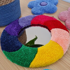 May include: A round mirror with a rainbow-colored frame made of fluffy yarn. The mirror is surrounded by a variety of colorful, fluffy flower shapes.