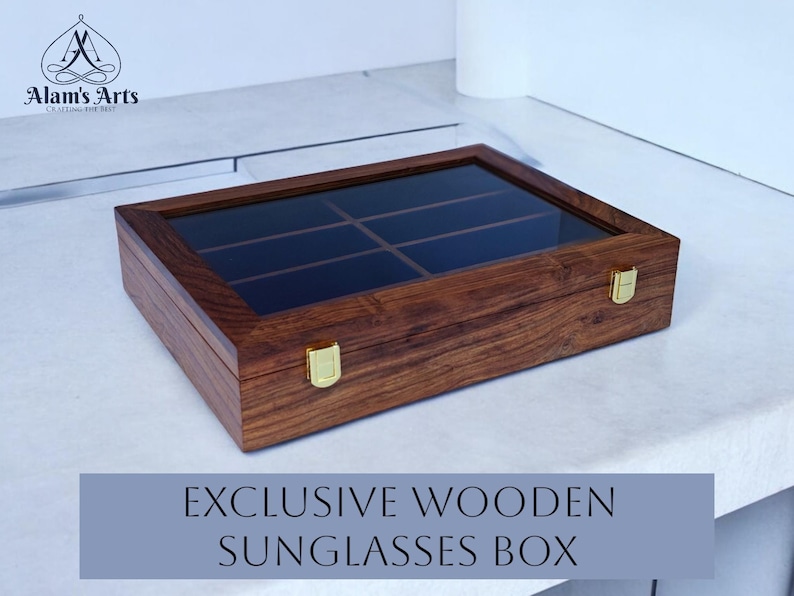 K&ouml;nnte beinhalten: Eine rechteckige Aufbewahrungsbox aus Holz mit dunkelbrauner Holzmaserung und einem transparenten Glasdeckel. Die Box verf&uuml;gt &uuml;ber sechs Innenf&auml;cher und zwei goldfarbene Metallverschl&uuml;sse an der Vorderseite. Das Logo Alam's Arts ist sichtbar.