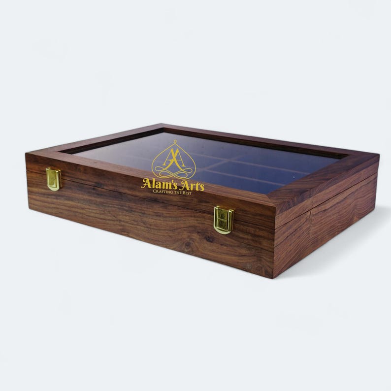 May include: A dark brown wooden box with a glass top and brass clasps. The box has a velvet interior and is designed to hold small items, such as jewellery or watches. The box has the text "Alam's Arts Crafting the Best" printed on the front.