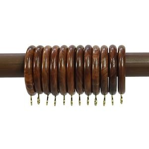 Może przedstawiać: Zestaw 15 drewnianych kółek do zasłon z złotymi haczykami. Kółka są ułożone na drewnianym drążku do zasłon.