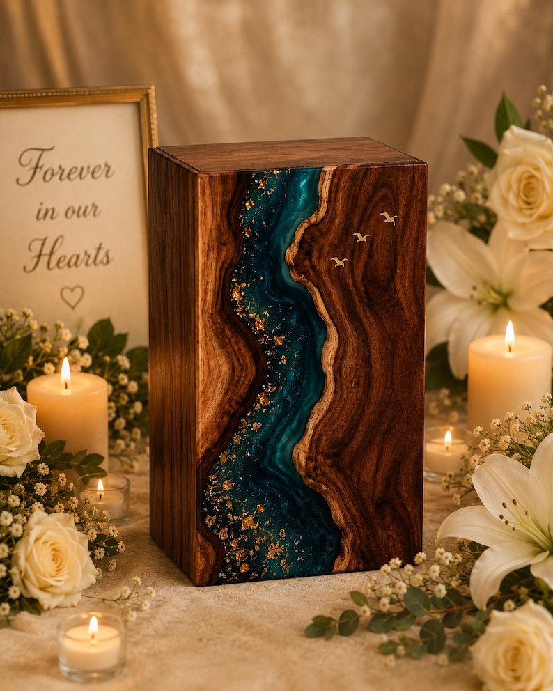 May include: A rectangular wooden cremation urn featuring a vertical river-like inlay of teal resin with gold leaf flakes. The dark wood grain contrasts with the smooth, glossy blue resin channel. Three small gold-colored bird silhouettes are embedded.