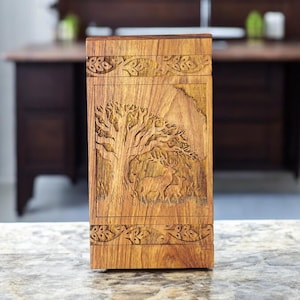 May include: A wooden box with a carved design of a tree and deer. The box is made of dark wood and has a natural finish.