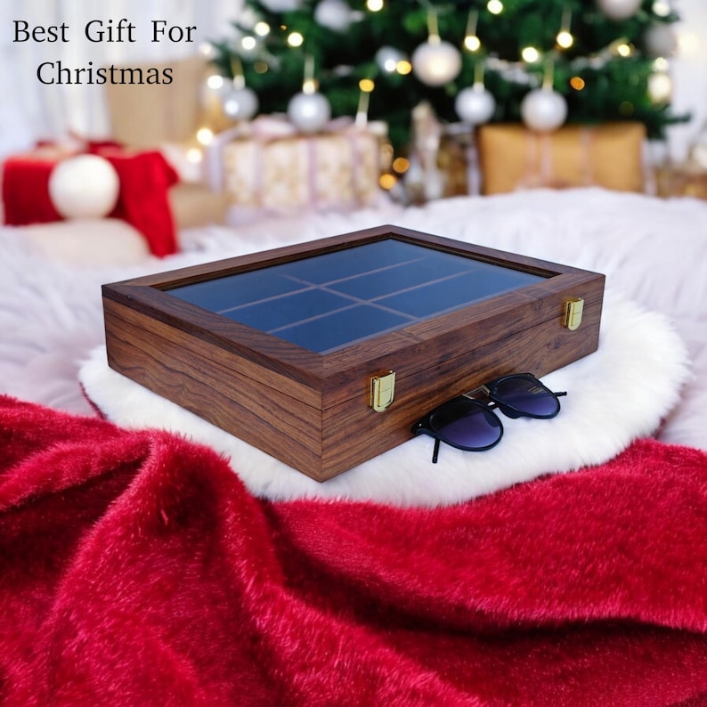 K&ouml;nnte beinhalten: Eine rechteckige Aufbewahrungsbox aus Holz mit Glasdeckel und goldfarbenen Metallverschl&uuml;ssen. Die Box hat eine dunkelbraune Holzmaserung und ist in neun F&auml;cher unterteilt. Eine schwarze Sonnenbrille liegt auf der wei&szlig;en Oberfl&auml;che.
