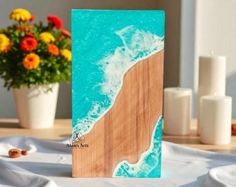 May include: A rectangular wooden art piece depicting a beach scene. The top half is turquoise resin, simulating ocean waves. The bottom half is natural wood, representing a sandy beach. The piece has the text "Alam's Arts".