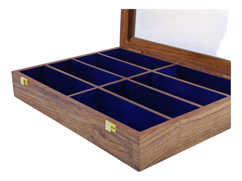 K&ouml;nnte beinhalten: Eine rechteckige Aufbewahrungsbox aus Holz mit einem aufklappbaren Glasdeckel und goldfarbenen Metallverschl&uuml;ssen. Der Innenraum ist in acht separate F&auml;cher unterteilt, die jeweils mit einem tiefblauen Stoff ausgekleidet sind.