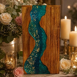 May include: A rectangular wooden serving board featuring a central, wavy river-like inlay made of deep teal resin. The resin section is embedded with shimmering gold leaf flakes, contrasting against the natural brown wood grain of the board.