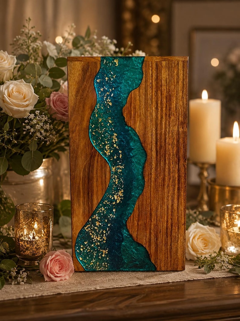 May include: A rectangular wooden serving board featuring a central, wavy river-like inlay made of deep teal resin. The resin section is embedded with shimmering gold leaf flakes, contrasting against the natural brown wood grain of the board.