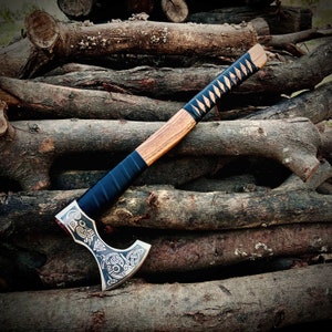 May include: A hand-forged axe with a wooden handle wrapped in black leather. The axe head features intricate carvings of a Viking knotwork design.