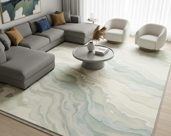 Puede incluir: Una alfombra rectangular grande con un diseño de acuarela en tonos azules, verdes y crema. La alfombra está en un salón, complementando un sofá seccional gris, dos sillones blancos y una mesa de centro redonda. Dimensiones: aproximadamente 300 cm x 200 cm.