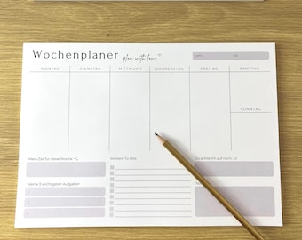 May include: A white weekly planner with the German word "Wochenplaner" at the top, along with the phrase "plan with love." A wooden pencil rests diagonally across the planner. The planner has sections for each day of the week.