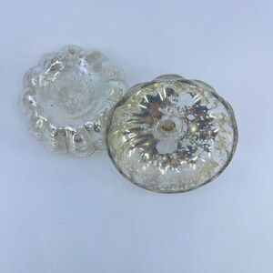May include: Two antique silver-coloured, pumpkin-shaped moulds. The moulds have a scalloped edge and a textured surface. The moulds are made of a shiny, reflective material, and are likely vintage kitchenware.