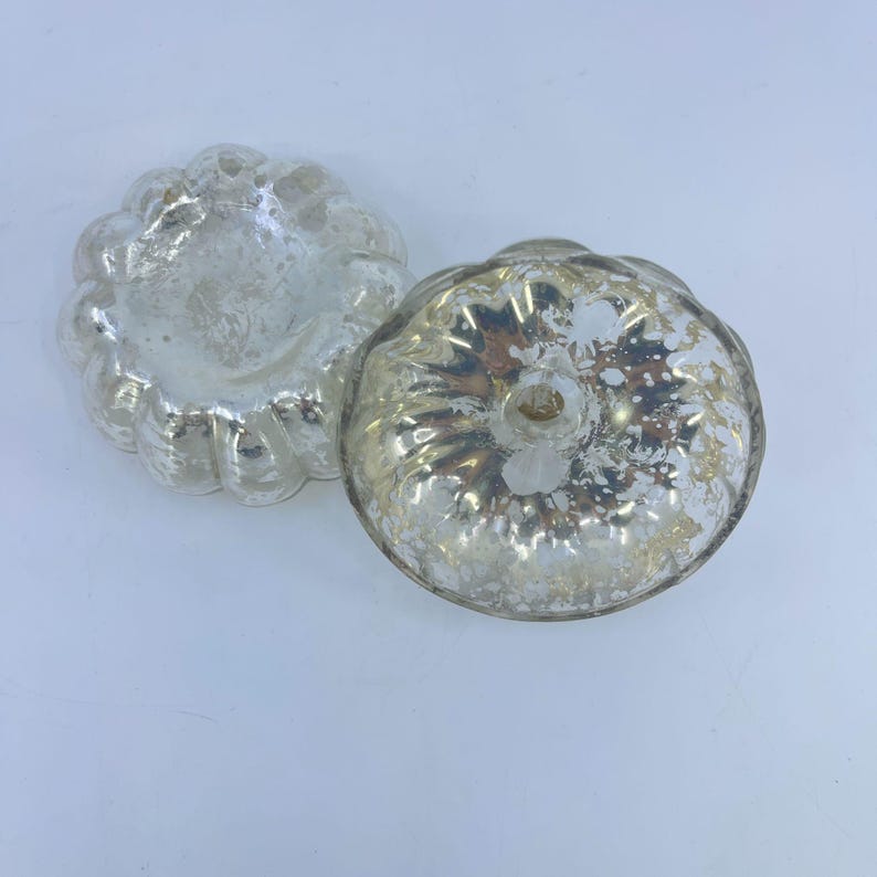 May include: Two antique silver-coloured, pumpkin-shaped moulds. The moulds have a scalloped edge and a textured surface. The moulds are made of a shiny, reflective material, and are likely vintage kitchenware.