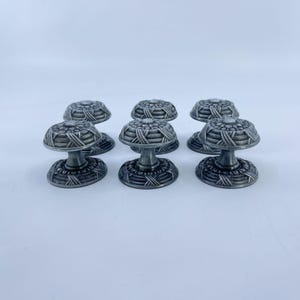 May include: A set of six round metal cabinet knobs with a dark silver finish. Each knob features a textured, woven-style pattern on the top surface and a matching circular base, connected by a smooth, tapered central post for mounting.