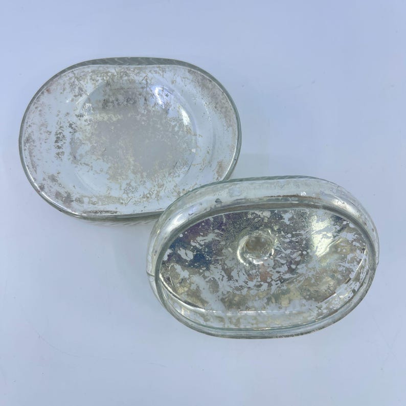 May include: Two oval-shaped, clear glass dishes with a distressed, silver-colored finish. The dishes have a shallow, bowl-like design and are likely decorative or for serving small items. The glass has a vintage, antique appearance.