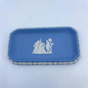 May include: A rectangular blue ceramic tray with a white relief design of figures playing musical instruments. The tray has a white decorative border and is likely used for serving or display.