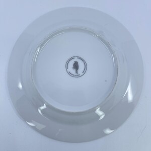 May include: White ceramic plate with a slightly raised rim. The center of the plate features a small, circular design with a bird silhouette and text. The plate is designed in Indonesia.