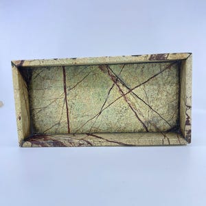 May include: A rectangular tray crafted from light green stone featuring prominent dark red and brown veining throughout the surface. The tray has thick, solid walls and a flat base, showcasing natural mineral patterns and textures.