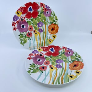 May include: Two white ceramic plates with a floral design. The plates feature a colorful watercolor-style pattern of red, purple, orange, and yellow flowers with green leaves. The plates are round and have a glossy finish.