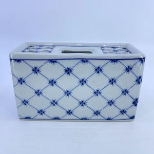May include: A rectangular white ceramic container with a blue floral pattern. The container has a lid with a rectangular opening and a series of small holes. The blue pattern is a repeating diamond grid with a floral design at each intersection.