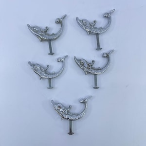May include: Five silver-colored dolphin-shaped drawer pulls with screws. The dolphin design features a curved body, a detailed face, and a curled tail. The pulls are arranged on a white surface.