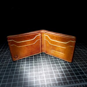 以下が含まれることがあります： 内側に「BOND LEATHER CO. ESTD. 2018」の文字が書かれた、赤いステッチの入った茶色の革財布です。