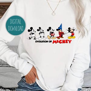 May include: White sweatshirt with a graphic of Mickey Mouse in different stages of his evolution. The text "Evolution of Mickey" is printed below the graphic.