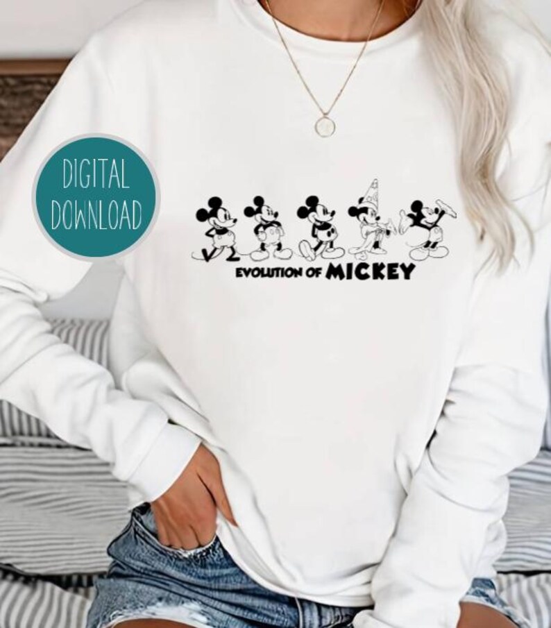 May include: White sweatshirt with a black and white graphic of the evolution of Mickey Mouse. The graphic shows Mickey Mouse in different stages of his design, from his earliest appearance to his modern look. The text "Evolution of Mickey" is printed below the graphic.